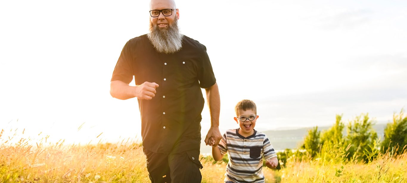 A man running in a field with his young child who has downs syndrome