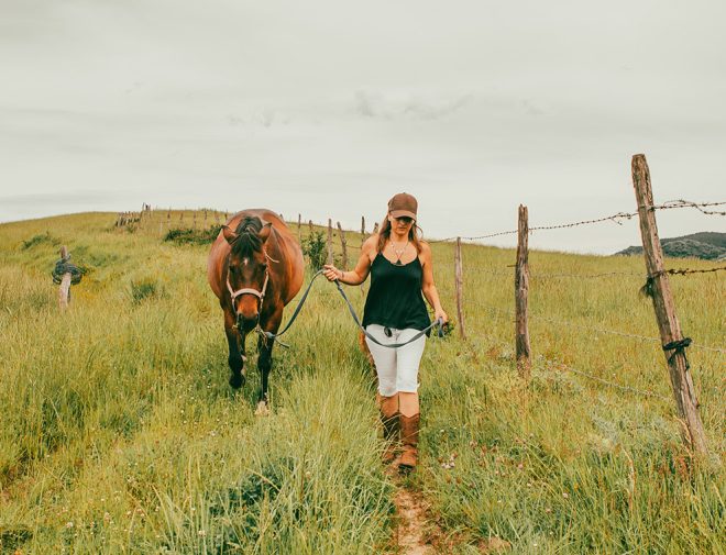 A woman walking a horse along a fence