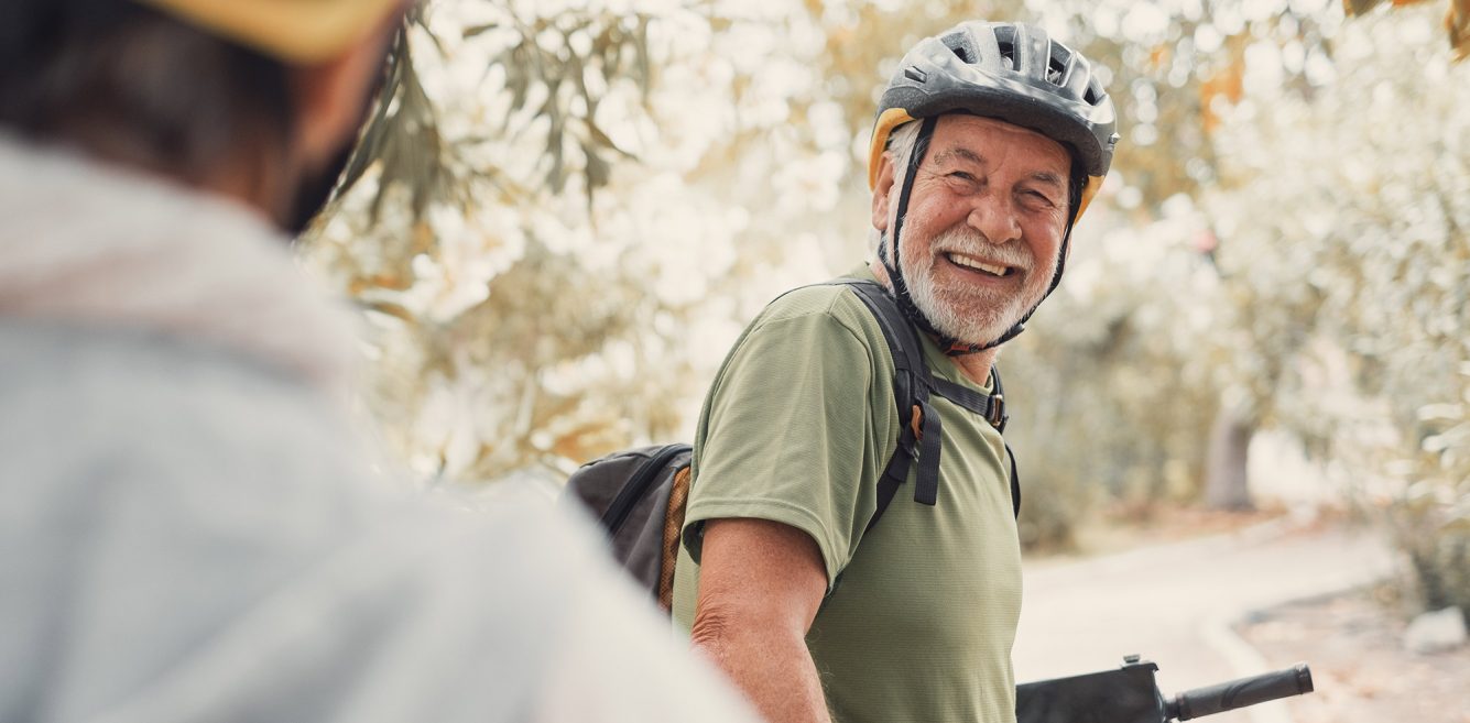 Older man in a bike helmet smiling at the person behind him