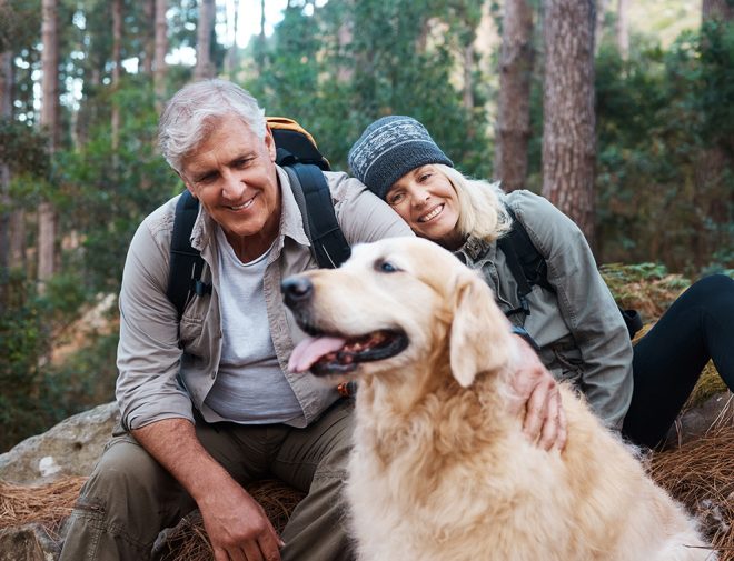 An older woman and a man taking a break on a hike with their elderly dog
