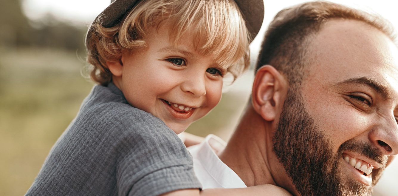 Man with a small blond boy in a hat riding on his back