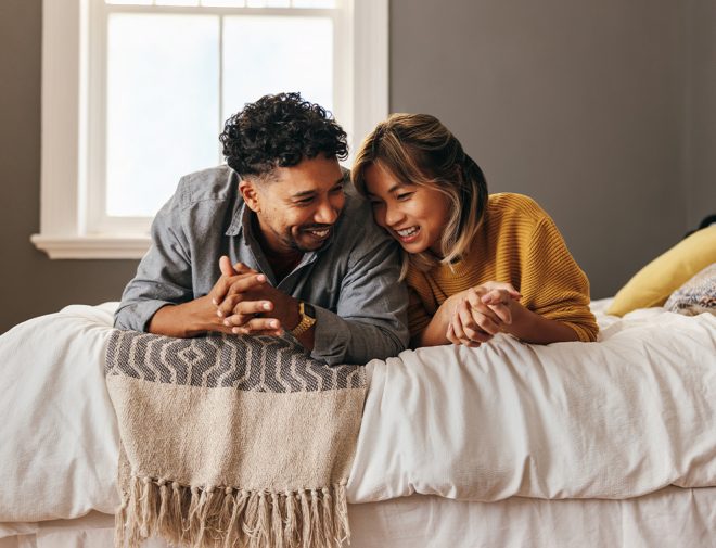 A young man and a woman laying on a bed smiling and laughing