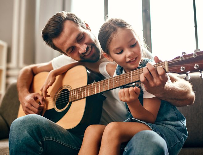 A man teaching his daughter how to play the guitar