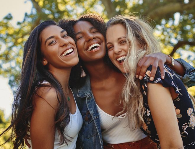 Three college-aged girls hugging and laughing