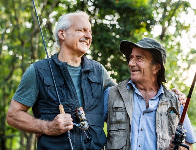 Two older men hugging and smiling in fishing gear