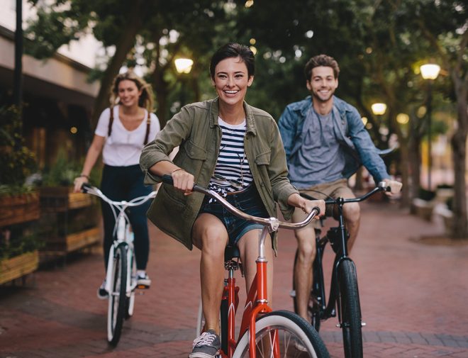 Three young adults riding bikes through a city and smiling