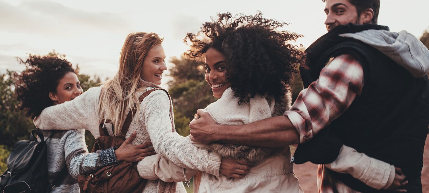 Four students with their arms around each other walking and looking behind them