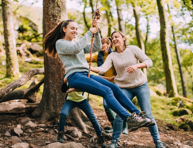 A young woman swinging on a rope swing with her family around her