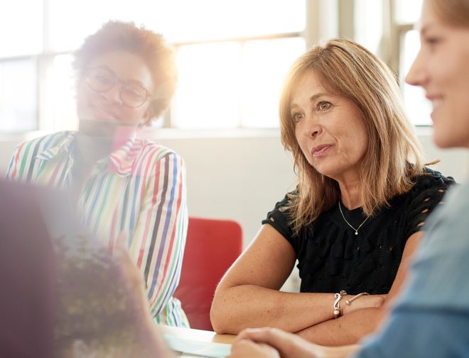 A middle-aged woman sitting at a table listening to someone speak