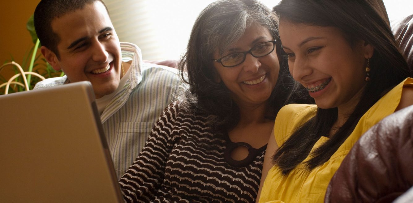 A family sitting on a couch and smiling with a laptop